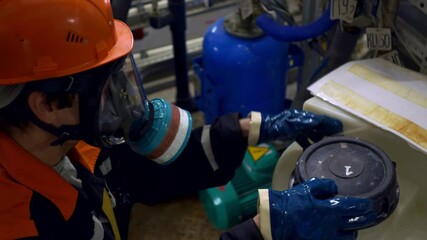 A laboratory assistant in the chemical industry in overalls, a gas mask and a work helmet, opens a vessel with dangerous pesticides. Dangerous work with toxic substances. Chemical industry accident