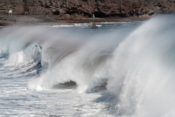 Seascape with strong waves and Neptune sculpture in the background in Melenara beach. Telde. Gran Canaria. Canary Islands