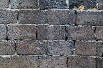 The background of an old, crumbling wall of stone blocks. The texture of a textured, ancient wall made of stone blocks bonded with cement mortar.