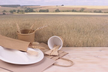 Paper disposable food  dishes on wooden table, grain wheat field background.Copy space