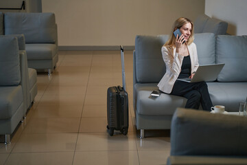 Female tourist with laptop having phone conversation in hotel lobby