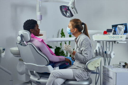Young woman working in a dentist’s office and talking with patient