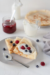 Thin pancakes with berries. White background. Nice breakfast. Pancakes with sour cream and raspberry jam.