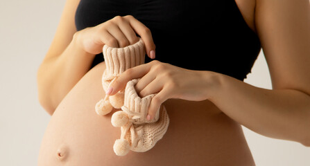 Small shoes for the unborn baby in the belly of pregnant woman. Close up. Motherhood, pregnancy,...