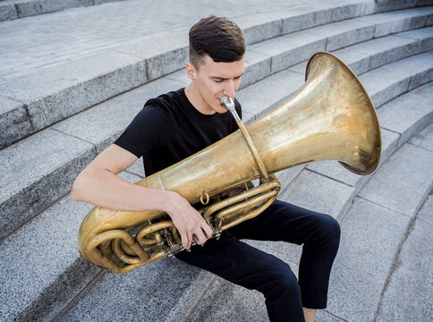 Young street musician playing tuba sitting on granite steps