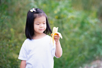 Happy child enjoy eating yellow banana. Asian girl sweet smiling.
