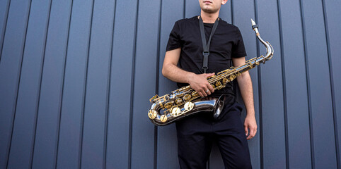 Young street musician playing saxophone near the big blue wall