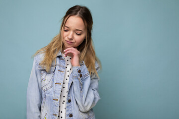 Photo of young sad upset beautiful blonde woman with sincere emotions wearing denim blue jacket isolated over blue background with copy space