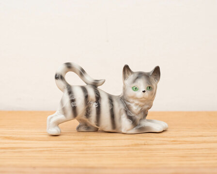 Porcelain cat figurine  on a wooden furniture behind white wall