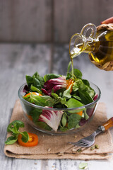 Healthy food. Green salad of herbs and vegetables in a transparent bowl with olive oil in a bottle on wooden board. Rustic. Background image, copy space