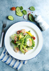 Healthy cuisine. Fresh green salad with seafood. Cucumber, avocado, spinach, herbs, tomatoes and shrimp with sauce on a white plate on a light gray background. Rustic. Background image, copy space