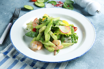 Healthy cuisine. Fresh green salad with seafood. Cucumber, avocado, spinach, herbs, tomatoes and shrimp with sauce on a white plate on a light gray background. Rustic. Background image, copy space