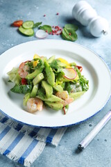 Healthy cuisine. Fresh green salad with seafood. Cucumber, avocado, spinach, herbs, tomatoes and shrimp with sauce on a white plate on a light gray background. Rustic. Background image, copy space