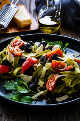 Spinach tagliatelle with parmesan, cherry tomatoes, black olives and basil on wooden table
