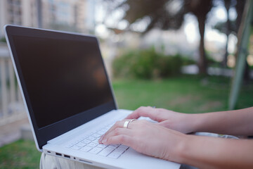 Female hands on laptop, woman types on keyboard sitting in park.