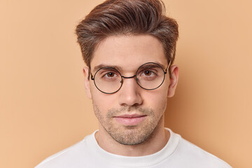 Serious looking macho man with hairstyle and stubble wears round spectacles listens carefully to...