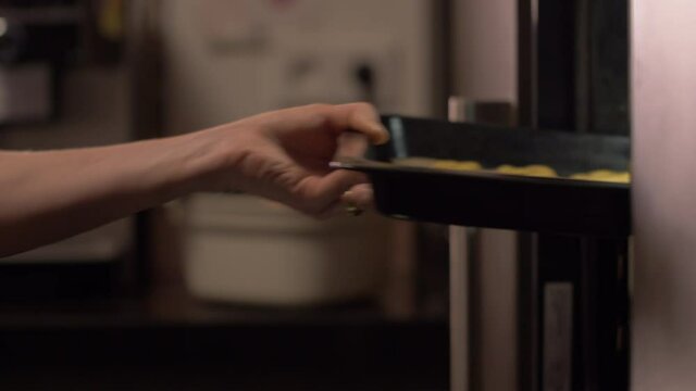 Side close up view, woman's arms opening oven door and putting tray into oven