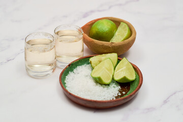 Shot of tequila with lime and salt on white background