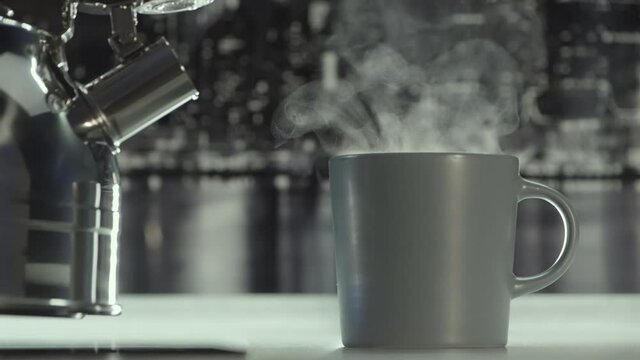 Close up of pouring hot boiled water from the polished steel gas kettle into the mug. Action. Cozy atmosphere in the kitchen in grey colors at home.
