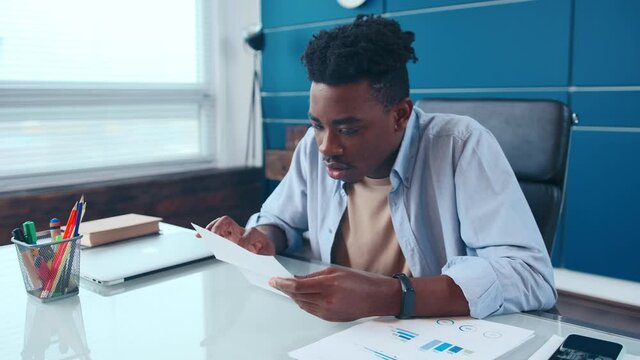 Excited African American male executive receiving mail with salary growth payment, business loan approval. Happy overjoyed man opening envelope reading great news in paper letter sitting at workplace.