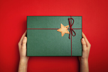 Hands holding Green present box on a red background.