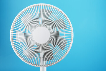 White modern electric fan for cooling the room on a blue background.