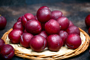 Fresh fruits of the ruby plum lie on a wicker tray.