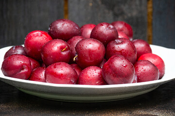 Fresh fruits of ruby plum on a white plate, served on a wooden table.