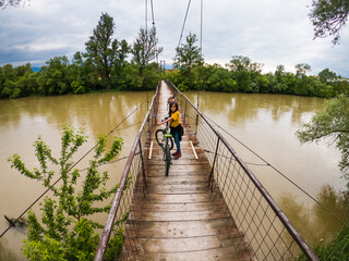 Boy crossing suspension bridge over yellow river with bike
