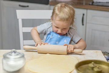 Little helper boy is rolling dough with a wooden rolling pin in domestic kitchen, indoors. Horizontally.