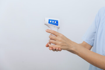 Temperature measurement gun in doctor hands. Close-up shot of doctor wearing protective surgical mask ready to use infrared isometric thermometer gun to check body temperature for virus symptoms
