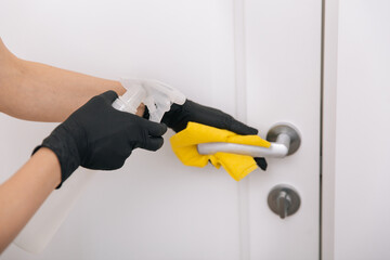 Cleaning door handle with yellow wipe in black gloves and sanitizer spray. Disinfection in hospital and public spaces against corona virus. Woman hand using towel for cleaning