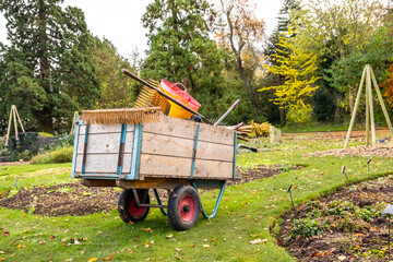 Wooden cart of gardening equipment and gardening tools among the flower beds and plant beds in Cambridge Botanical Gardens - obrazy, fototapety, plakaty