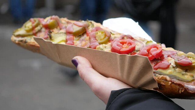 Female hand holding delicious sandwich called Zapiekanka, near Okrąglak street food court on Plac Nowy (Jewish Square). Kazimierz district of Old Town Krak&oacute;w, famous Zapiekanki Krakowskie.