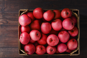 Red apples in a box on a wooden table, top view.