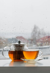 cup of  tea on windowsill with autumn leaves on window pane