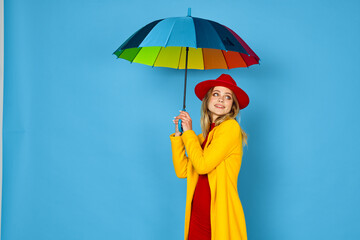 woman in yellow coat multicolored umbrella posing blue background