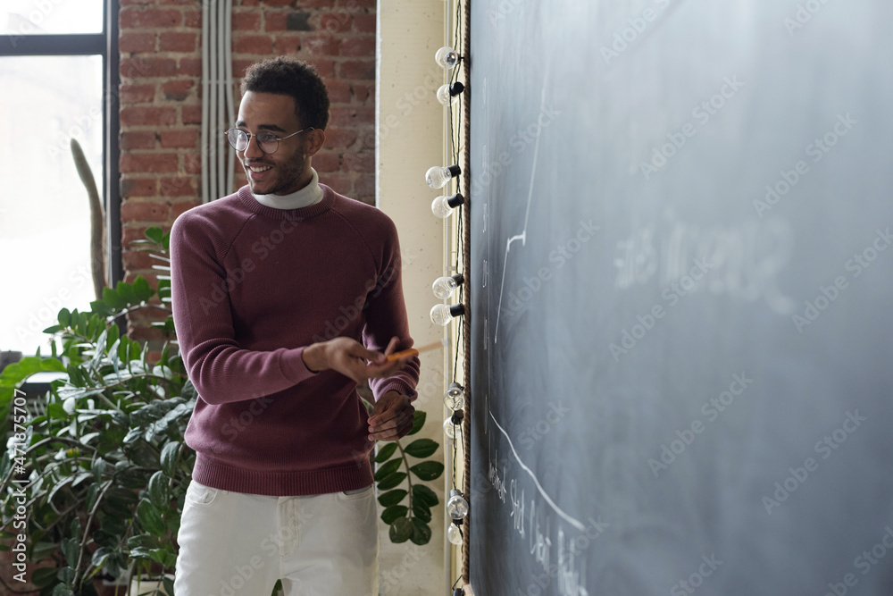 Poster young successful economist in casualwear explaining financial data or graph to colleagues while poin