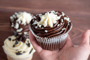 Delicious fresh cupcake with dark and white chocolate in your hand. Side view, blurred background, selective focus. Desserts, sweets, high-calorie foods