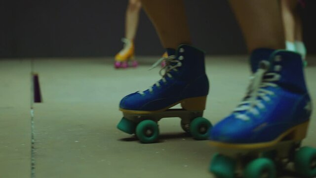 Female legs in roller blades, skating fast at the roller park on floor . Close-up legs of young women is professionally skating . Different kind of and colorful vintage roller blades . Slow Motion