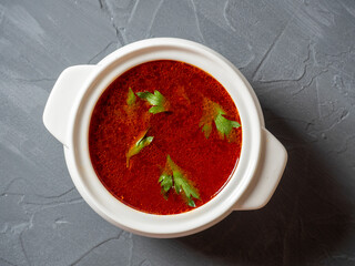 Close-up of soup borscht in a white ceramic soup bowl on a gray textured background. Traditional soup for Russia and Ukraine. Greens float on top of the soup. Top view