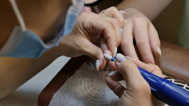 The master of the nail service removes the old gel polish shellac from the nails with a manicure machine. Slow motion, close-up.