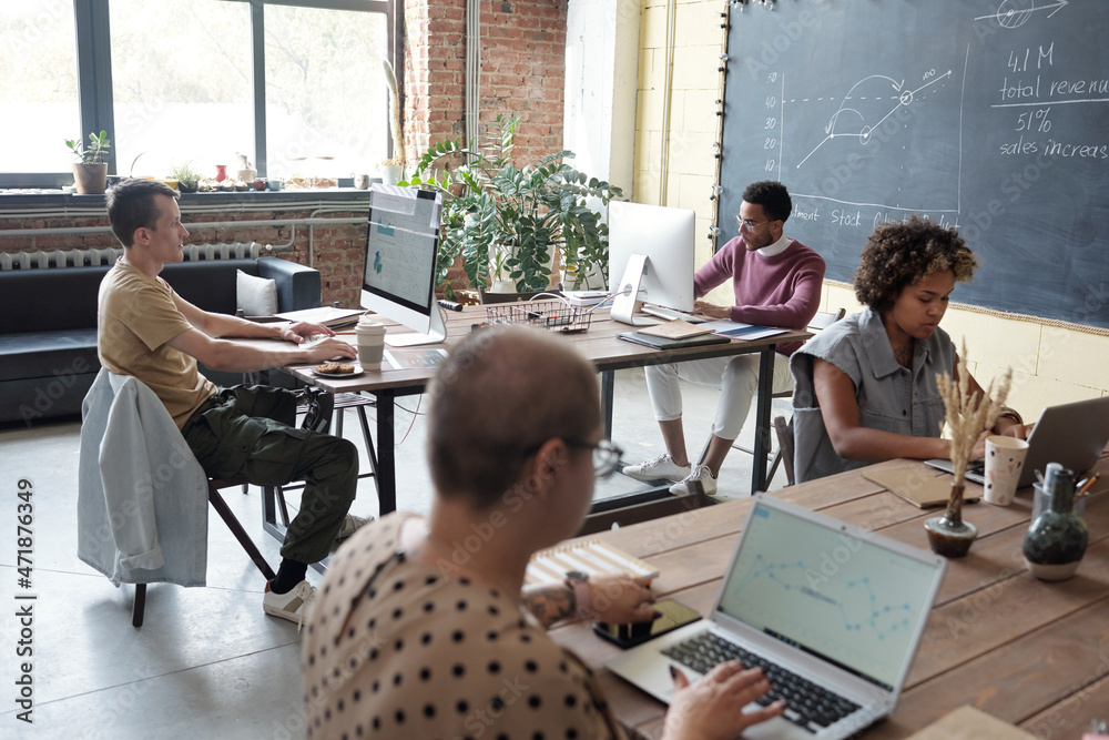 Poster Group of young contemporary economists working with financial data while sitting by tables in front of computers in office