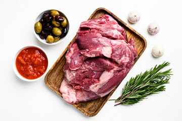 A large piece of raw meat, with ingredients and herbs, on white stone table background, top view...