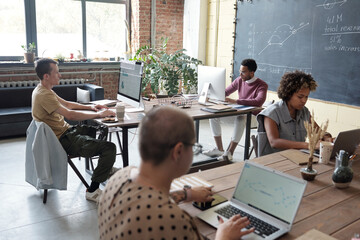 Group of young contemporary economists working with financial data while sitting by tables in front...