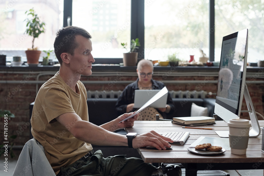 Poster SIde view of serious young businessman looking at computer screen while analyzing financial data against female colleague