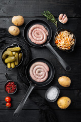 Traditional German Sausages with Mashed Potatoes and Sauerkraut in cast iron frying pan, on black wooden table background, top view flat lay