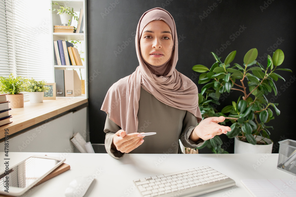 Poster young confident woman in hijab explaining subject to student while sitting in front of computer duri