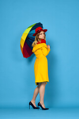 woman in yellow coat multicolored umbrella posing blue background