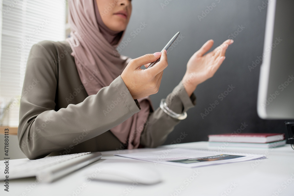 Aufkleber Hands of young teacher in hijab explaining something in front of computer while inetracting with online audience